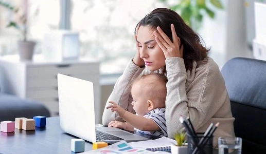 Photo d'une femme qui est devant son ordinateur en train de travailler, tout en ayant son bébé sur les genoux