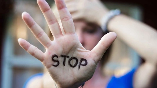 Photo d'une femme se tenant la tête et affichant le mot STOP écrit dans la paume de sa main, contre la charge mentale